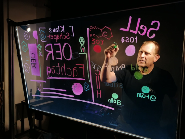 Klaus Schaper vor einem Lightboard, auf welches er Begriffe notiert (z. B. OER).