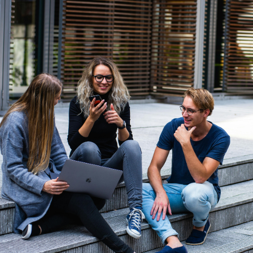 Drei Studierende sitzen auf einer Treppe und unterhalten sich.