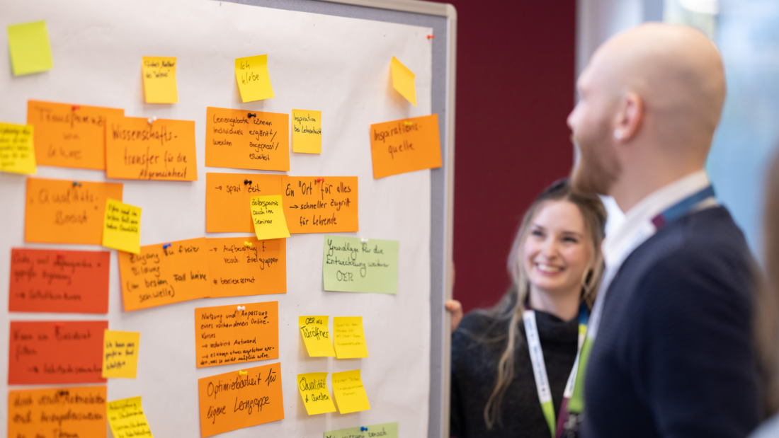 Post-its an einer Wand, Anne Mainz und Tom Strube schauen auf die Wand.